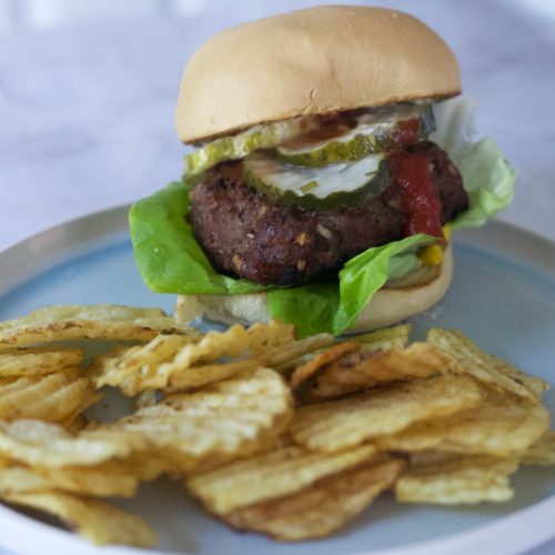 thick bison burger patty with mustard, ketchup, buns and a side of chips