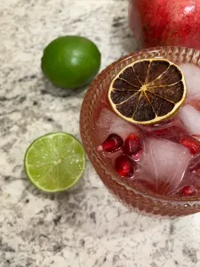 pomegranate mocktail in a cocktail glass with limes and pomegranate on the side