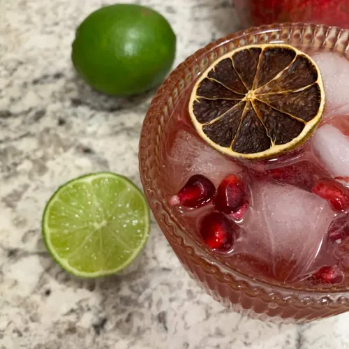 pomegranate mocktail in a cocktail glass with limes and pomegranate on the side