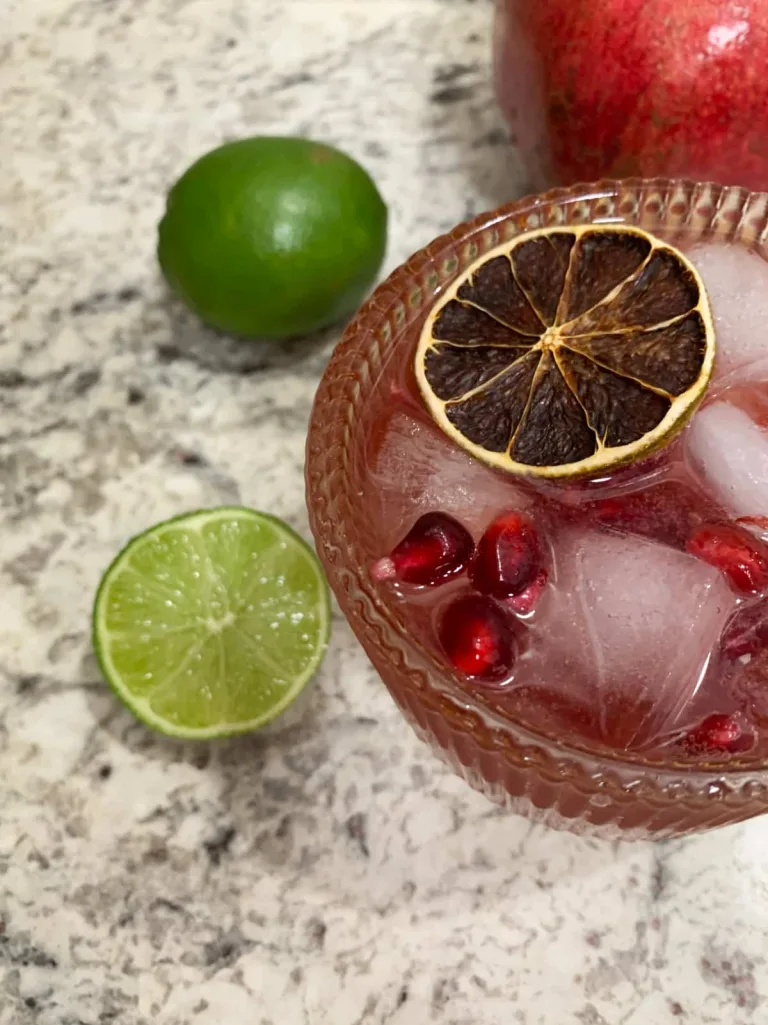 pomegranate mocktail in a cocktail glass with limes and pomegranate on the side