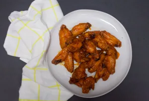 wings on a plate with a sticky orange buffalo sauce on top