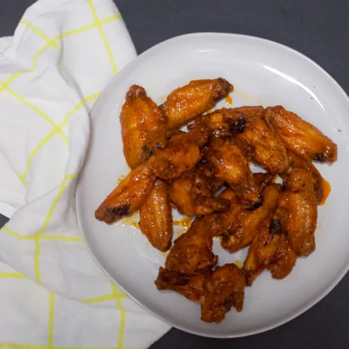 wings on a plate with a sticky orange buffalo sauce on top