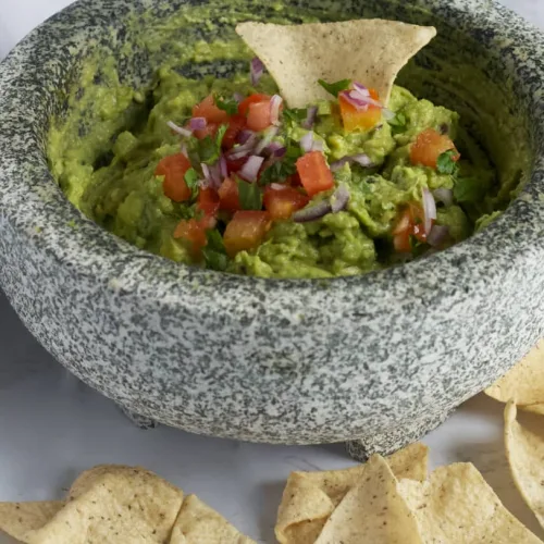 bright green chunky guacamole in a mortar and pestle with chips surrounding it.