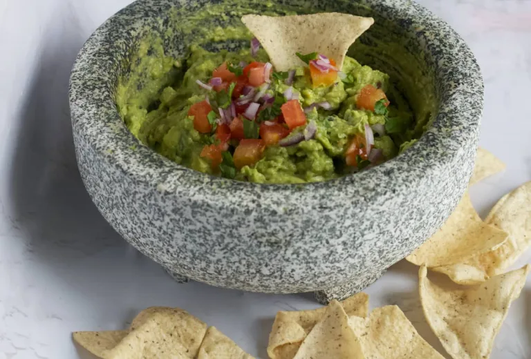 vibrant green gaucamole in a mortar and pestle and tortilla chips on the side