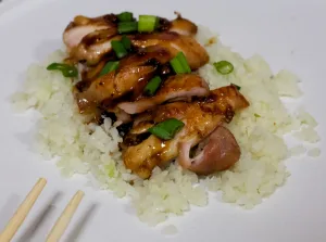 Paleo saucy teryaki chicken on top of cauliflower rice with chopsticks