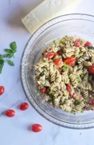 pesto pasta salad with tomatoes on the side, fresh basil and a hunk of parmesan