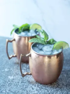 copper mugs filled with ice and moscow mule ingredients, garnished with a slice of lime and fresh mint sprig