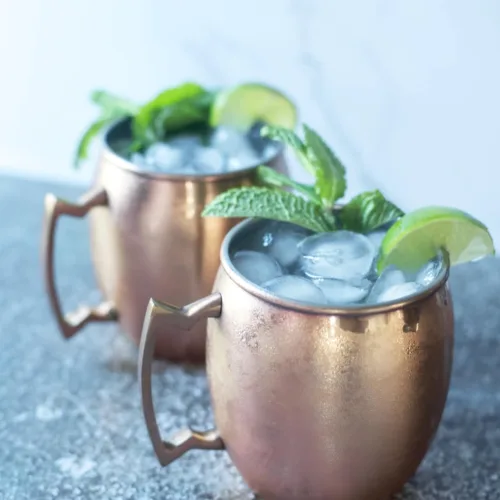 copper mugs filled with ice and moscow mule ingredients, garnished with a slice of lime and fresh mint sprig
