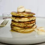 loight fluffy pancakes stacked with sliced banana on top
